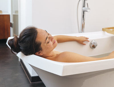 Une femme aux cheveux bruns et au chignon se d&eacute;tend dans sa baignoire. 