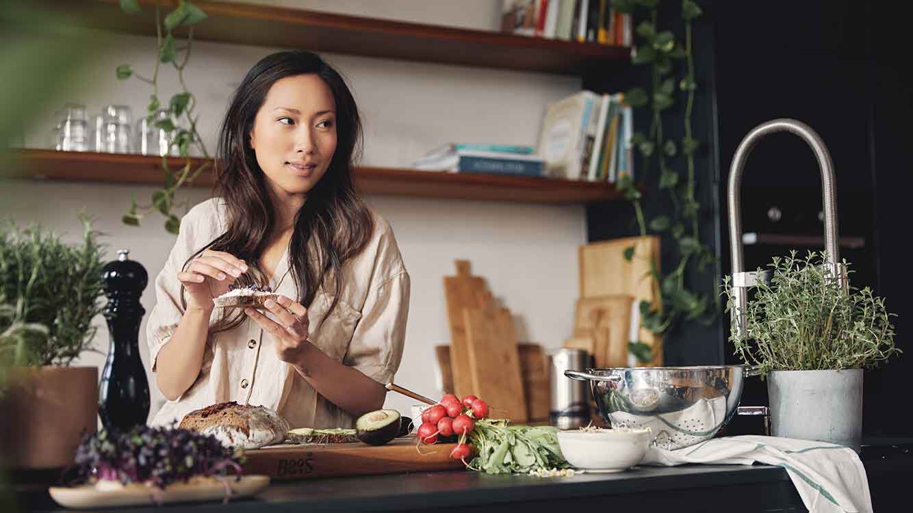 Femme à un coin cuisine avec de la nourriture à la main. 