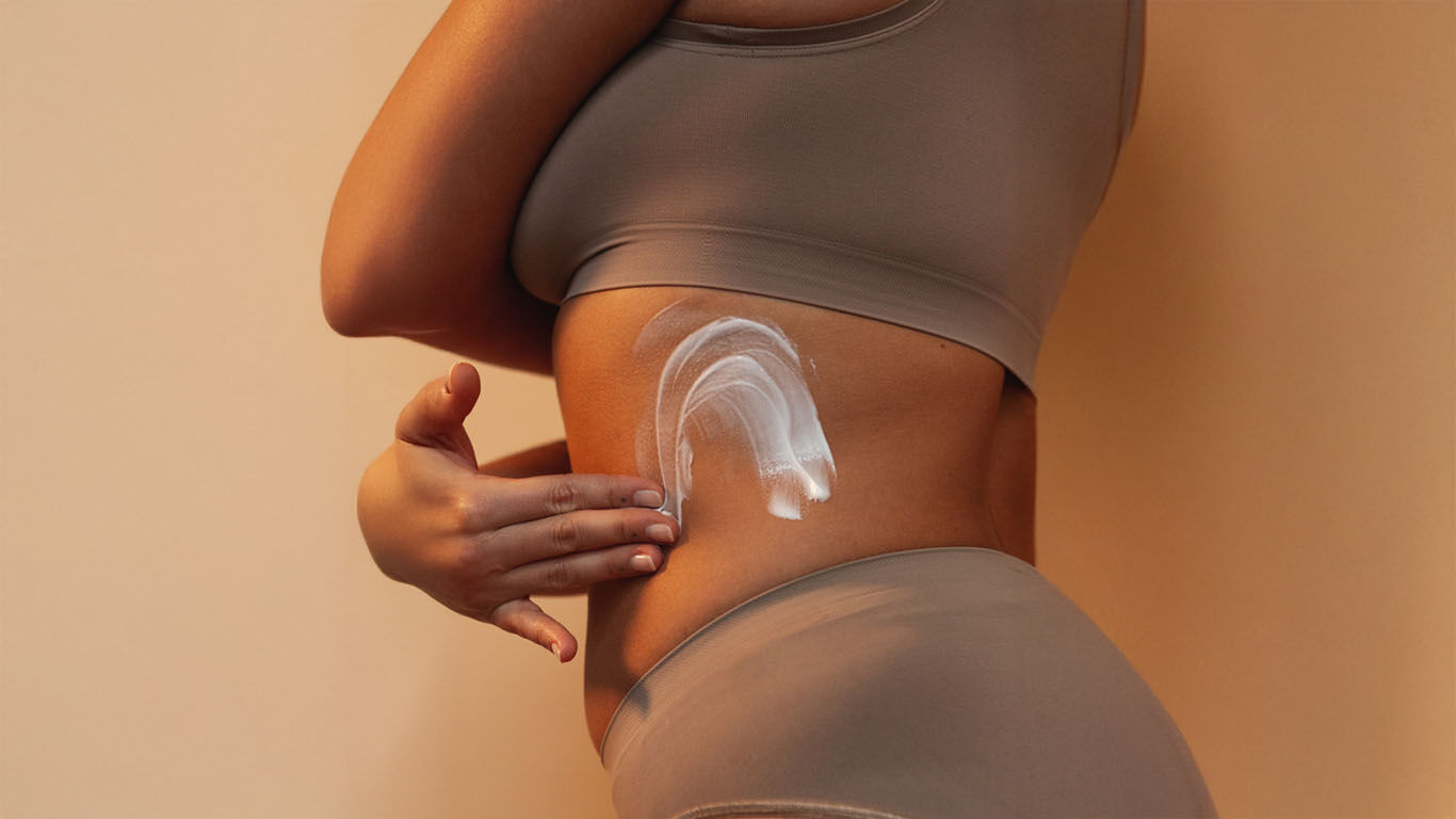 Gros plan sur une femme qui s'applique de la crème sur le ventre 