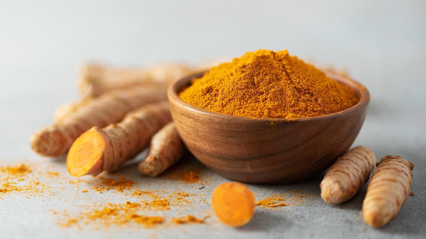 Le curcuma est posé à côté d'un bol de poudre de curcuma.