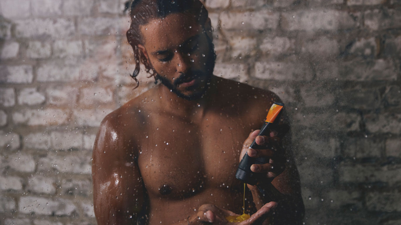 L'homme se tient sous la douche et presse le gel douche du tube dans sa main.