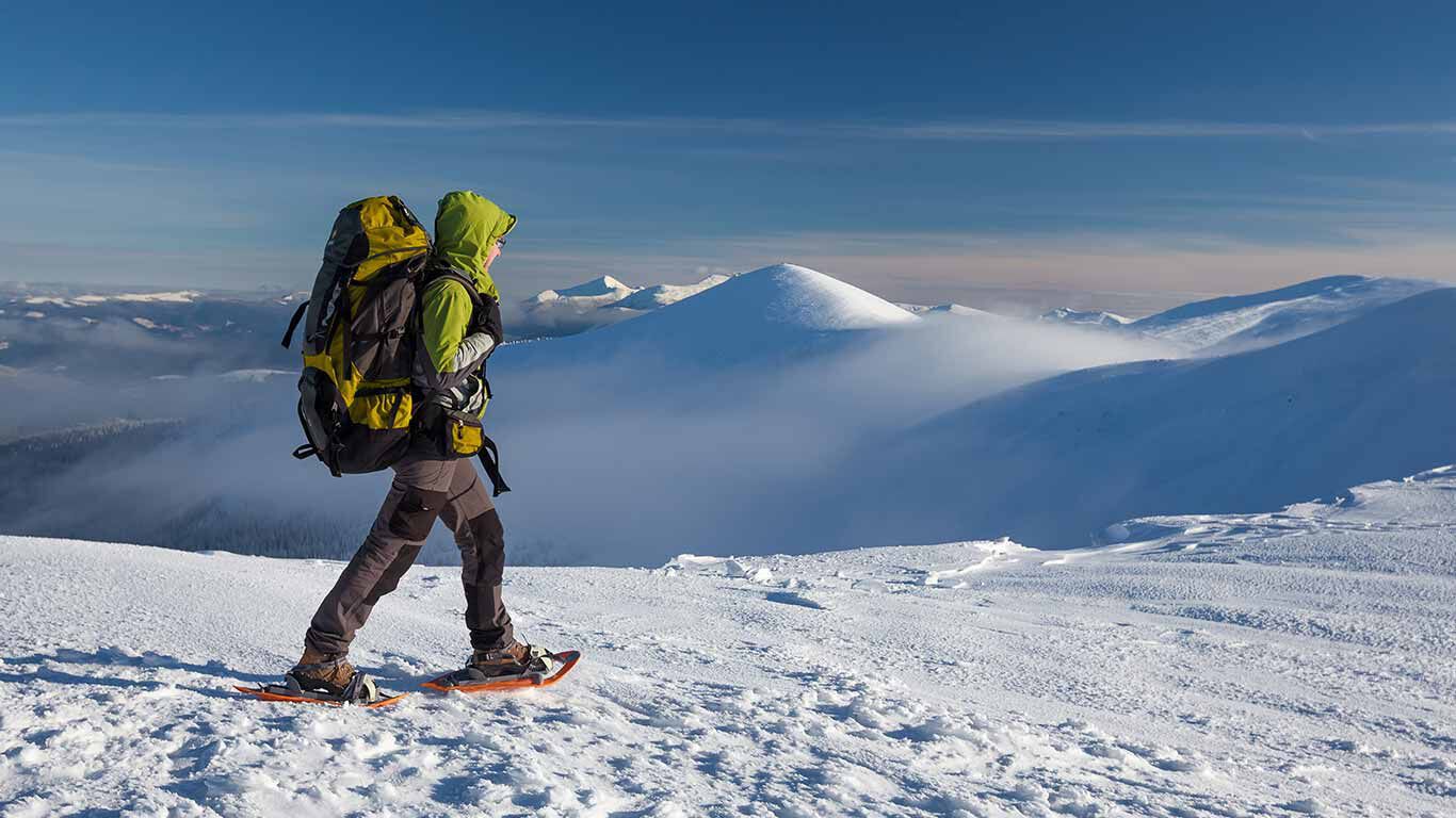 Personne effectuant une randonnée en raquettes à neige à hauteur des sommets de montagne avec un sac à dos.