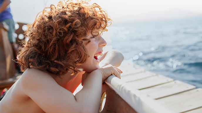 Garçon roux aux cheveux bouclés pointant au-dessus d'un bastingage de bateau.