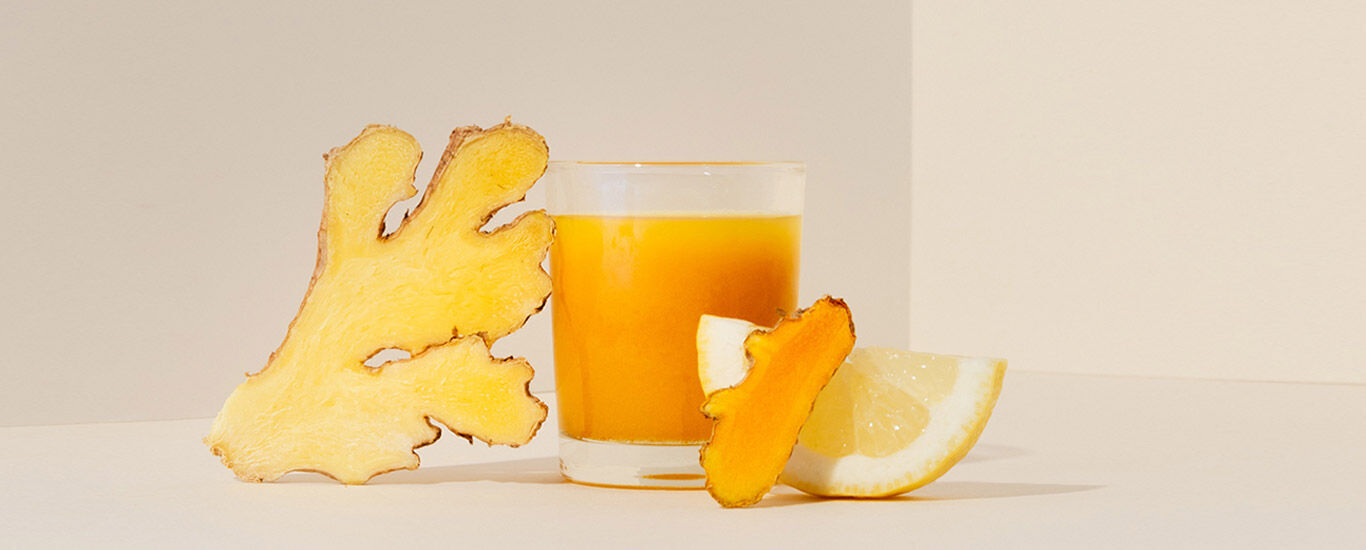 Immunbooster Ingwer-Shot Verre rempli d'un shot au gingembre. Ingrédients à côté : gingembre, curcuma, citron.