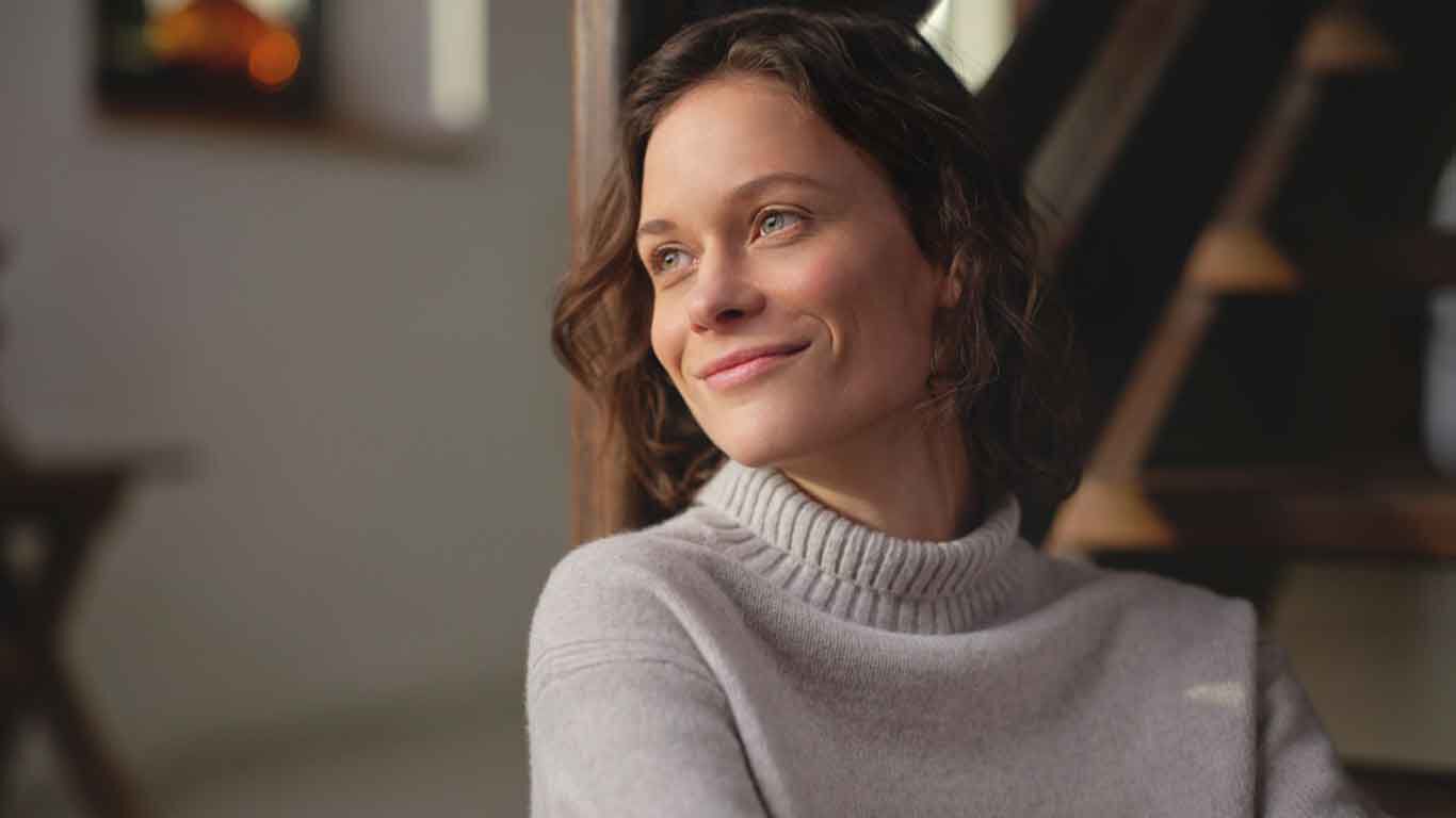 Gros plan sur une femme v&ecirc;tue d'un pull &agrave; col roul&eacute;. Elle porte un regard satisfait vers l'horizon. 