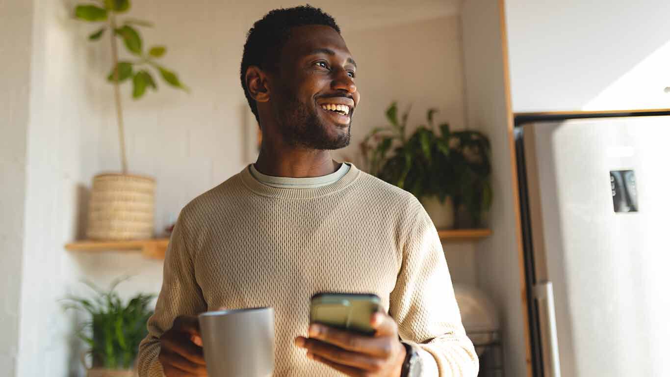 Homme souriant avec un téléphone portable et une tasse de thé à la main