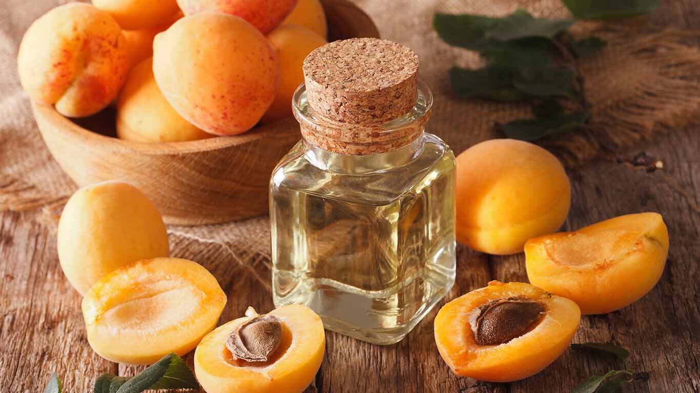 Une bouteille en verre d'huile de noyau d'abricot est posée sur une table avec des abricots entiers et coupés.
