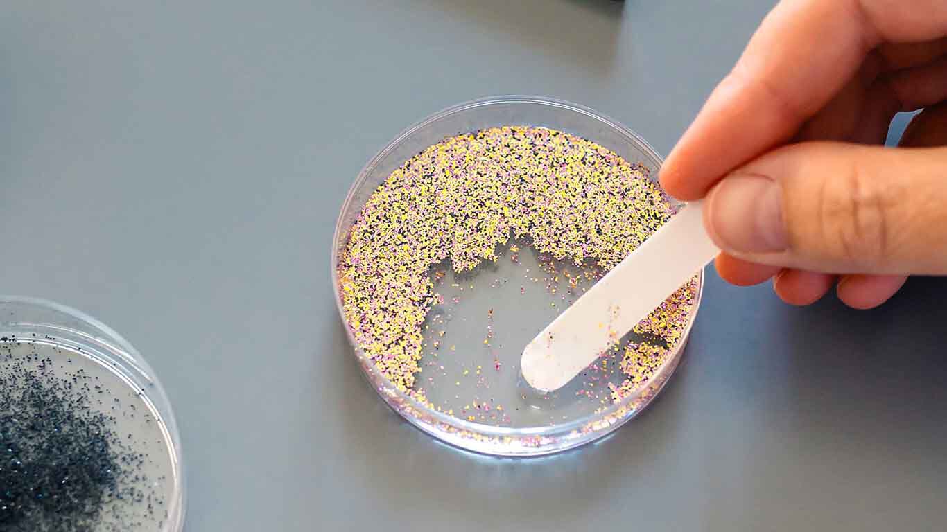 Gros plan sur des particules de microplastiques pr&eacute;sentes sur l'index et le majeur d'une personne.