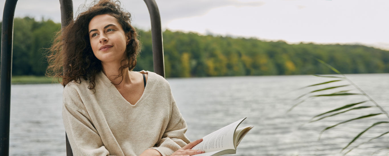Une femme se détend avec un livre au bord du lac. 