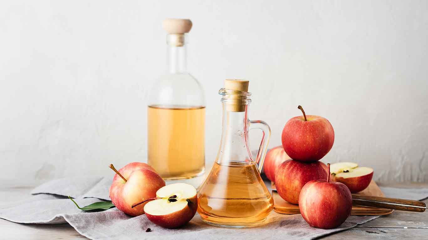 Verre de vinaigre de cidre, à côté de pommes.
