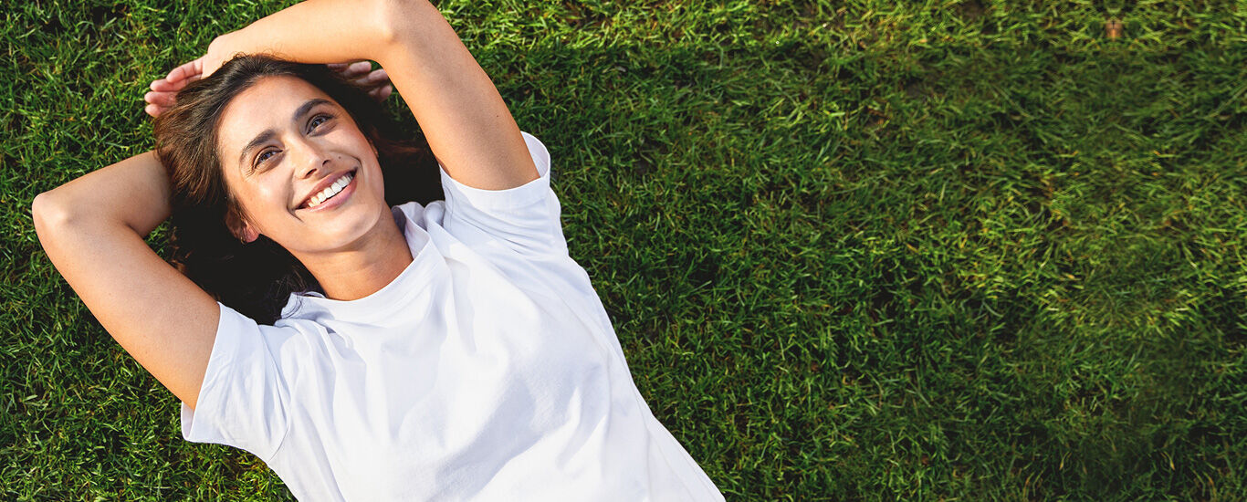 Newsletter Femme allongée sur le dos dans une prairie en riant