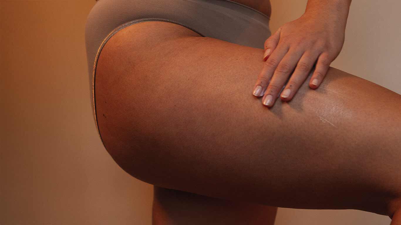 Photo de profil : femme appliquant de la crème sur sa cuisse. 
