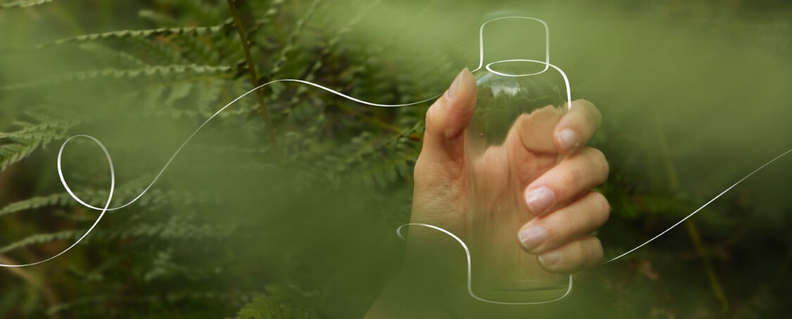 Ruka drž&iacute;c&iacute; nakreslen&yacute; obal Kneippova koupelov&eacute;ho oleje na zelen&eacute;m lesn&iacute;m pozad&iacute;.