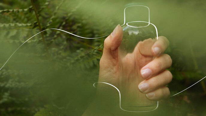 Ruka drž&iacute;c&iacute; nakreslen&yacute; obal Kneippova koupelov&eacute;ho oleje na zelen&eacute;m lesn&iacute;m pozad&iacute;.