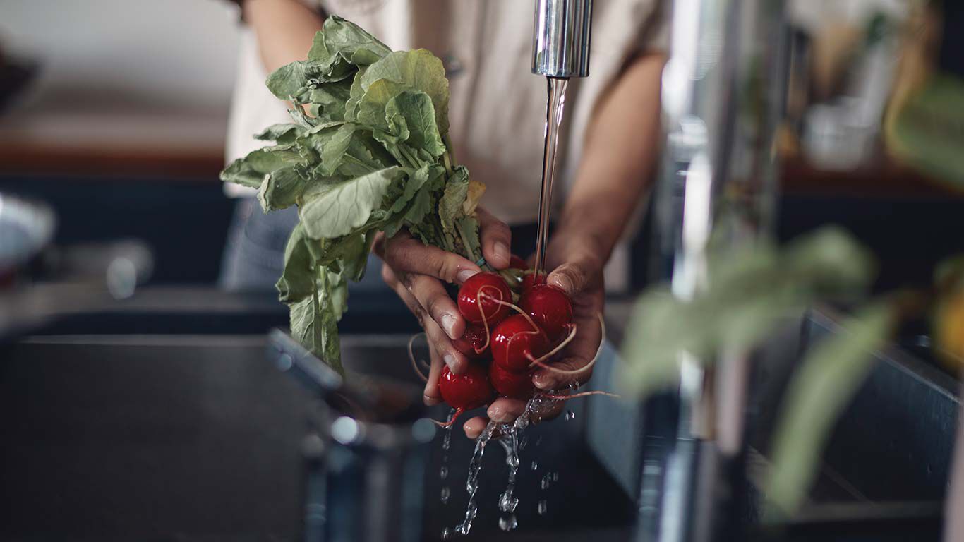 Žena myje ředkvičky pod tekouc&iacute; vodou.