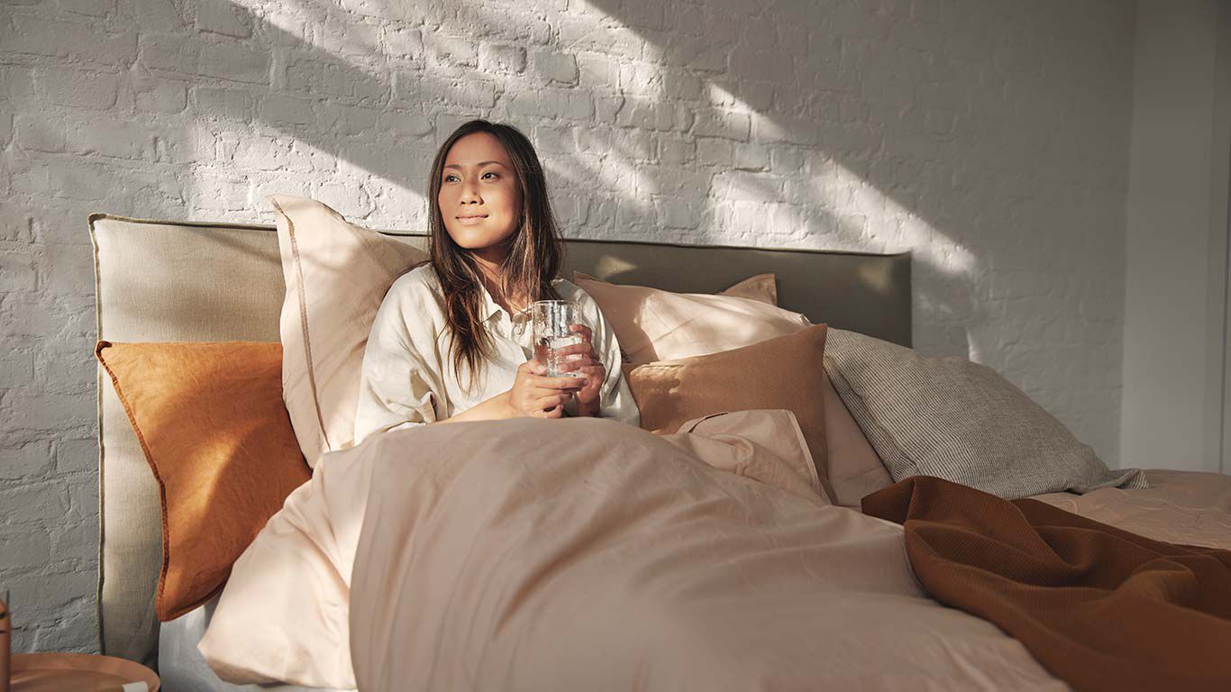 Mujer sentada en la cama con un vaso de agua.