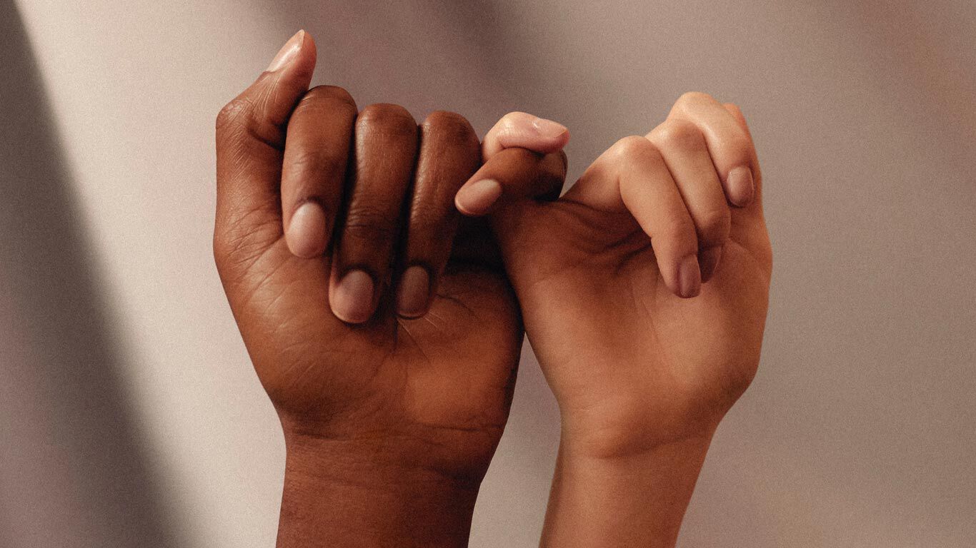 Dos manos de diferente color de piel, con los dedos entrelazados en señal de amistad.