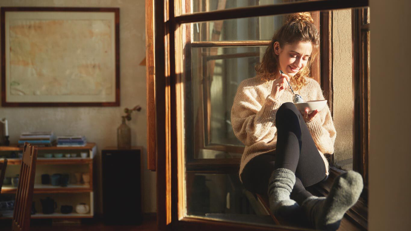 Mujer sentada en el alféizar de la ventana con ropa cómoda comiendo cereales