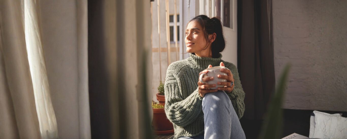 Mujer tomando una infusi&oacute;n sentada mirando a trav&eacute;s de la ventana