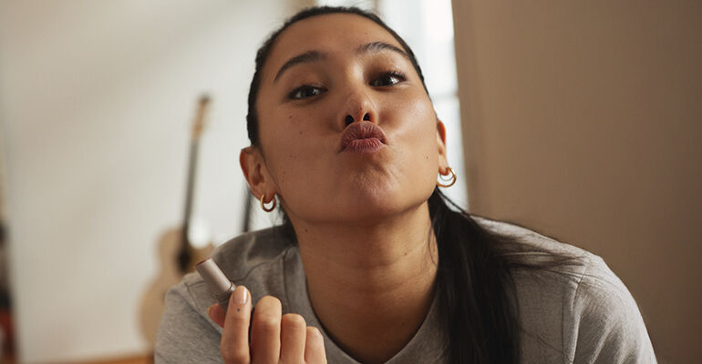 guia-hidratacion-labios mujer con labial en la mano y enseñando los labios pintados por el mismo