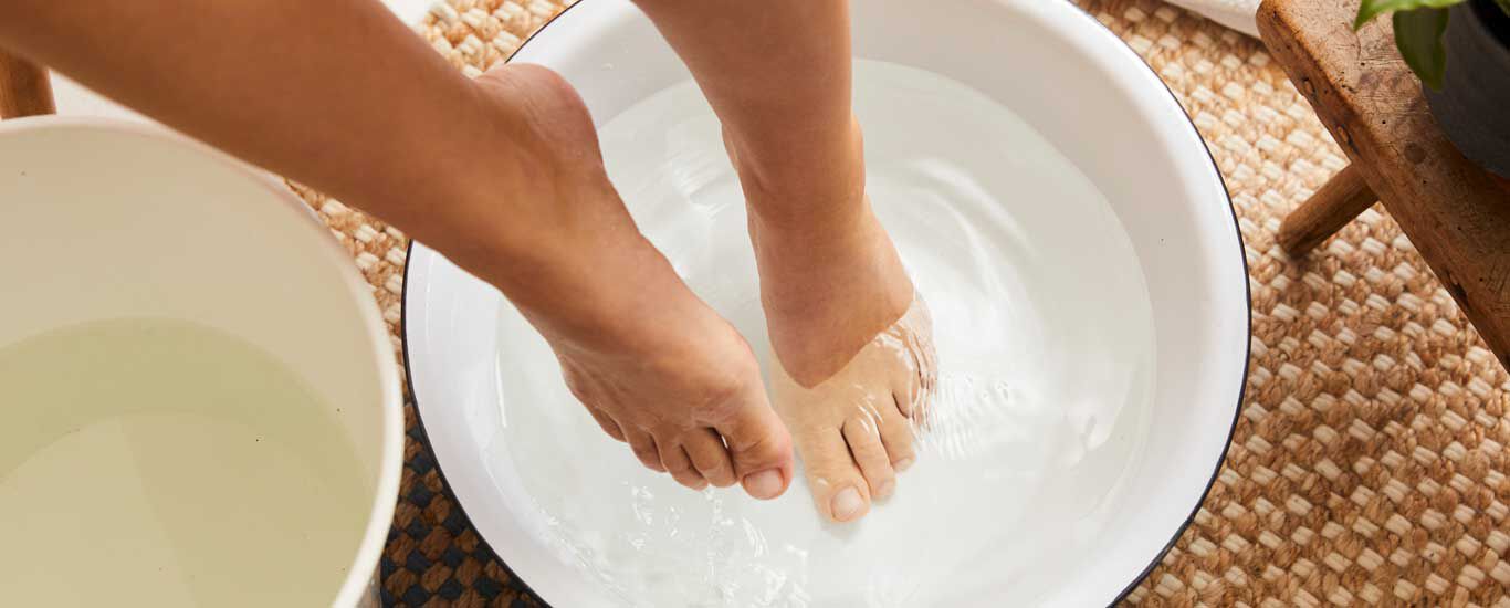 Gros plan sur deux pieds, dont l'un est dans une bassine remplie d'eau. À côté se trouve un seau rempli d'eau.