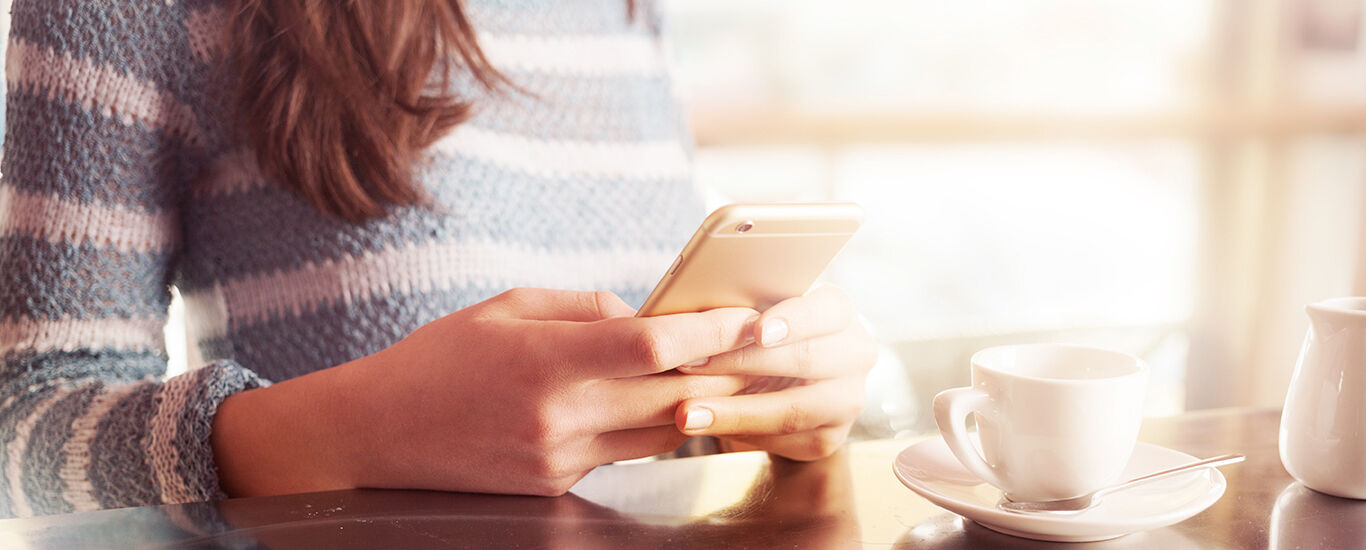 お問い合わせ頂き、ありがとうございます。 テーブルに座ってスマートフォンを操作する女性。