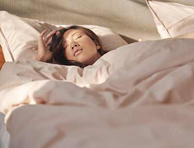 ベッドに横になって寝ている黒髪の女性。