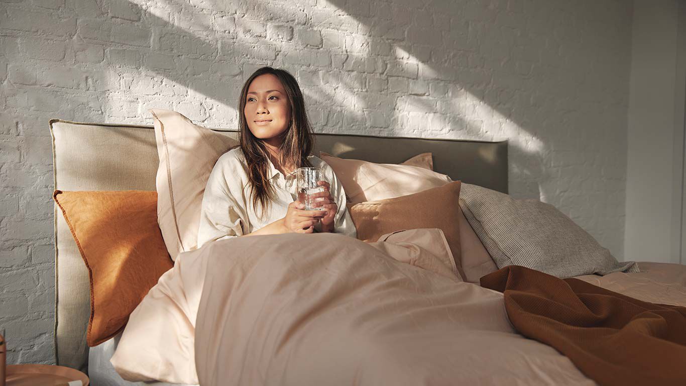 ベッドに座り、水を飲む女性。