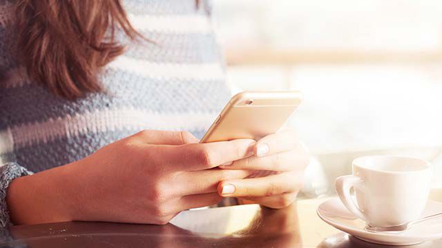 お問い合わせ頂き、ありがとうございます。 テーブルに座ってスマートフォンを操作する女性。