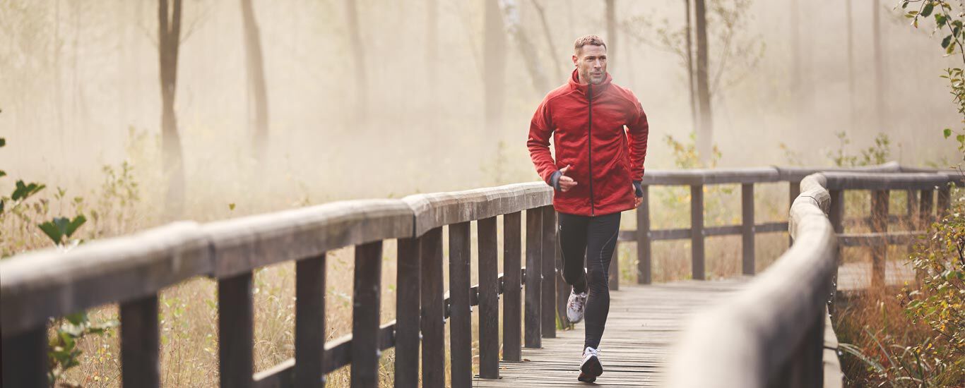 クナイプコラムの動き自然の中で木製の橋をジョギングで渡る男性。