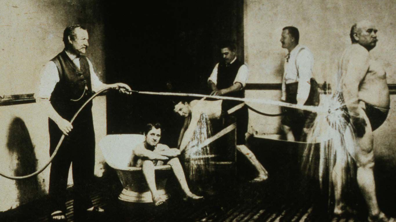 Czarno-białe zdjęcie XIX-wiecznej łaźni: kilku mężczyzn bierze prysznic Kneippa.